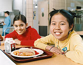 Allied Health jobs image of two children smiling while eating lunch together in the cafeteria